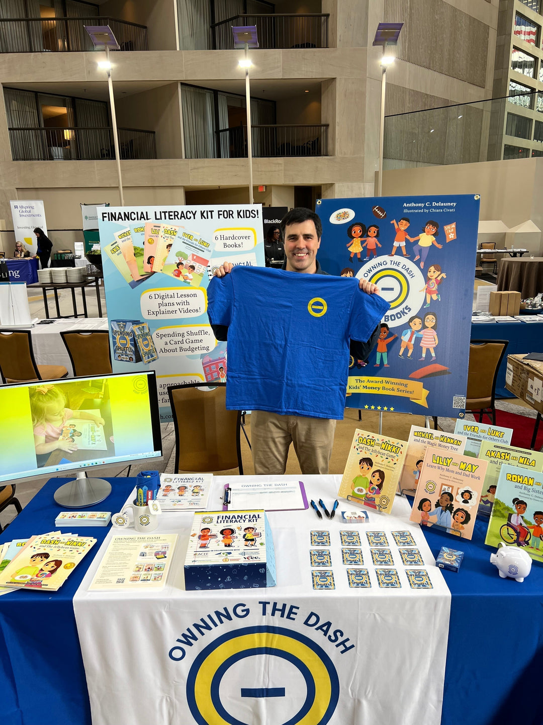 Tony holds up a blue Owning the Dash shirt at a booth